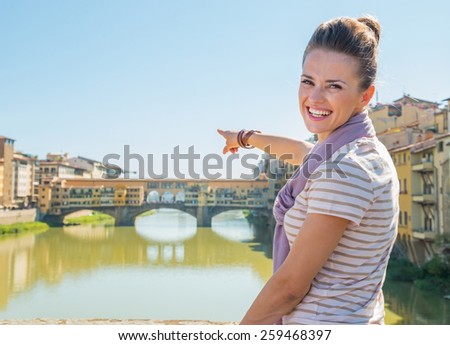 Happy young woman pointing on ponte vecchio in florence, italy