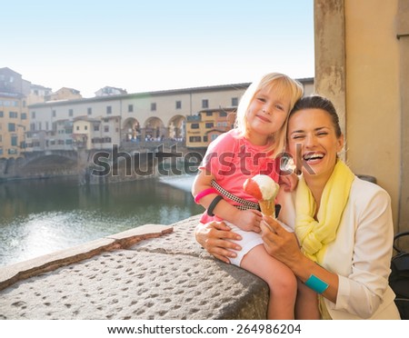 Portrait of happy mother and baby girl eating ice cream near ponte vecchio in florence, italy
