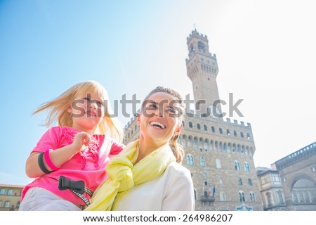 Happy mother and baby girl looking into distance in front of palazzo vecchio in florence, italy