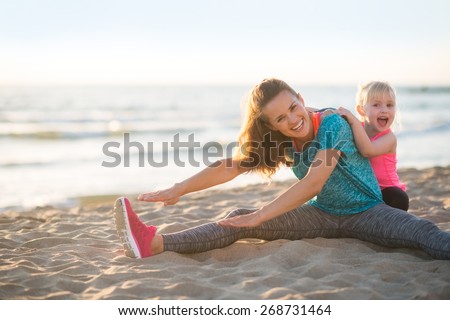 Healthy mother and baby girl stretching on beach in the evening