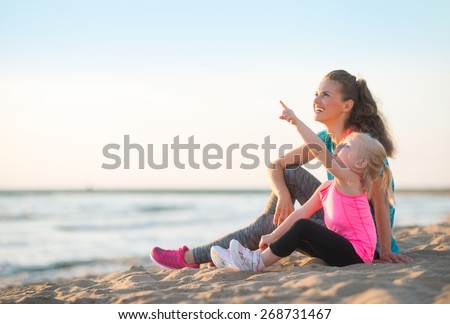 Healthy mother and baby girl pointing while sitting on beach in the evening