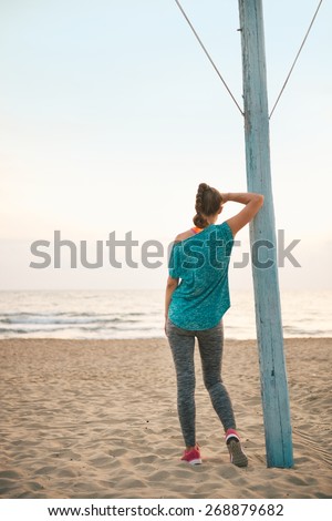 Fitness young woman on beach in the evening looking into distance. rear view