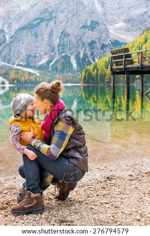 A kneeling mother and standing child wearing outdoor gear are giving Eskimo kisses on the shores of Lake Bries.