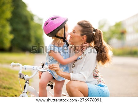 Eskimo kisses between a proud mother and daughter, who has just learned how to ride her bicycle. The mother kneels lovingly next to her daughter, holding her gently.