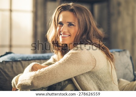 Close-up of elegant, smiling brunette woman, hugging her knees. Dressed casually, she is relaxing. Retro chic ambiance and cozy atmosphere.