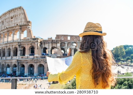 On hot summer's day, a woman is seen from behind and is holding a map of Rome. She is looking out onto Rome's Colosseum and the tourist crowds below.
