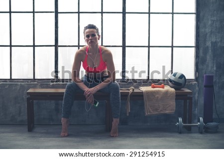 Resting her elbows on her knees, a young, athletic woman is sitting relaxing, resting in between workouts...