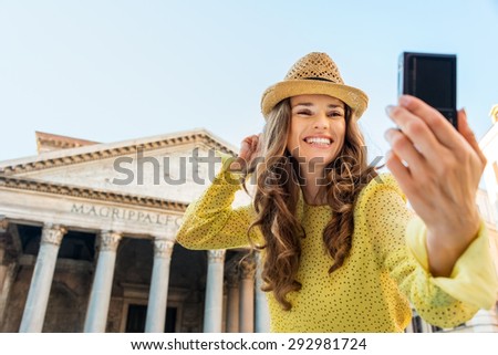 A woman tourist smiles as she is taking a selfie, cheering as she is standing near the Pantheon in Rome on a summer\'s day.