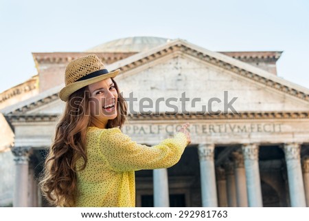 A young brunette woman smiles as she is pointing at the Pantheon in Rome.