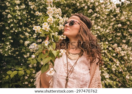 Longhaired hippy-looking young lady in knitted shawl and white blouse enjoying flowers fragrance