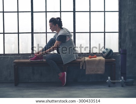 A quiet moment to tie her shoes. A fit, sporty young woman has one foot up on a bench, tying her shoelaces, as she gets ready to start her workout.