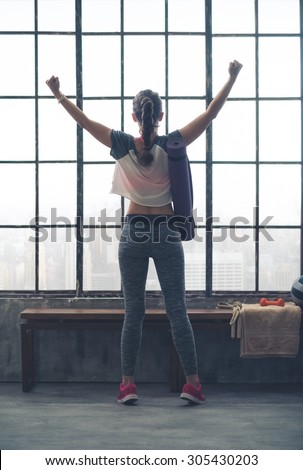 YES. I did it. I beat my goal! A young, fit woman rejoices in what she has achieved in her workout. Looking out on the city below her, she feels powerful and strong.