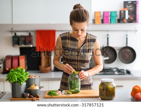 An elegant woman stands in her kitchen, at the counter, hard at work preparing dill pickles.