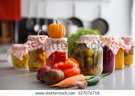 Oh, the tasty, crunchy treats that people will be feasting on in the winter, thanks to all of these preserved and pickled vegetables in glass jars. On the kitchen counter, fresh seasonal vegetables.