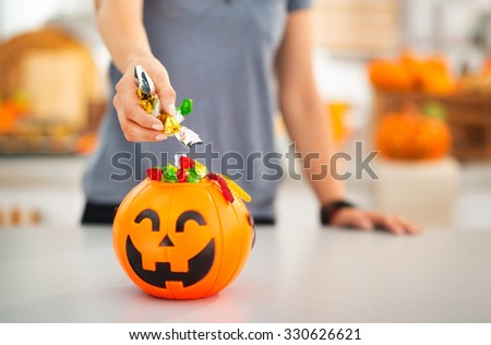 Halloween candy is never too much! Closeup on woman putting trick or treat candy in halloween Jack-o-Lantern bucket. Traditional autumn holiday