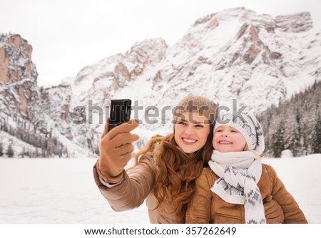 Winter leisure time spent outdoors among snowy peaks can turn the holidays into a fascinating journey. Mother and child taking selfie outdoors among snow-capped mountains