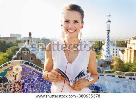 Refreshing promenade in unique Park Guell style in Barcelona, Spain. Happy young woman holding tourist guide and listening audioguide while in Park Guell, Barcelona, Spain