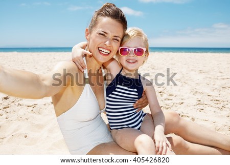 Family fun on white sand. Smiling mother and daughter in swimsuits taking selfies at sandy beach on a sunny day