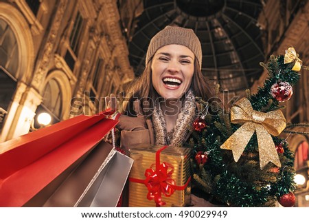 On a huge Christmas sales in Italian fashion capital. Portrait of cheerful elegant woman with Christmas tree and shopping bags in Galleria Vittorio Emanuele II in Milan, Italy