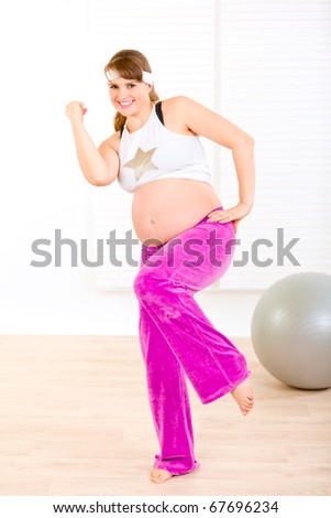 Smiling beautiful pregnant woman doing fitness exercises at living room