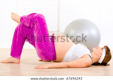 Smiling beautiful pregnant female making gymnastics  at home