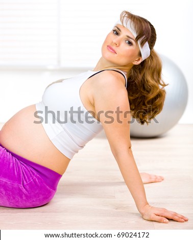 Smiling beautiful pregnant woman sitting on floor at home and relaxing after exercising