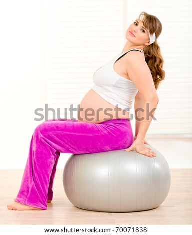 Smiling beautiful pregnant woman doing pilates exercises on gray ball