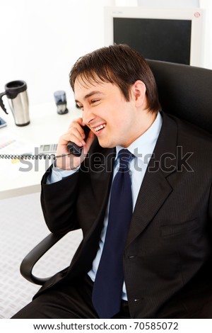 Smiling young business man talking on  telephone in office