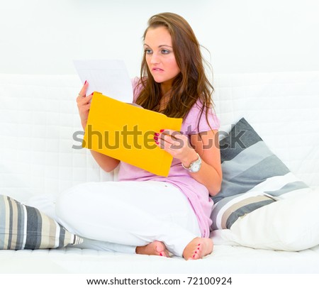 Sad woman sitting on couch at home  and reading bad news