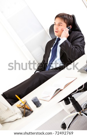Friendly  business man sitting in office with feet on desk and talking on mobile phone