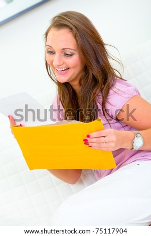 Pleased pretty woman sitting on sofa at home  and reading  letter