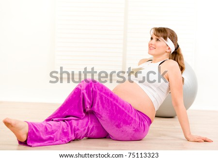 Smiling beautiful pregnant female making gymnastics  at home