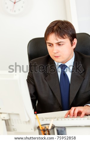 Concentrated modern business man sitting at office desk and working on computer