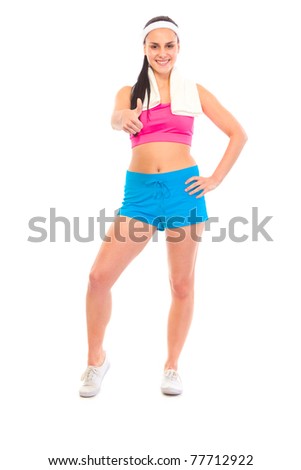 Smiling fitness girl with towel around neck showing thumbs up gesture isolated on white