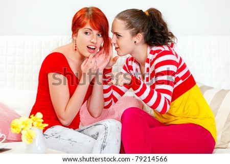 Girl whispering gossips in ear of her interested girlfriend and pointing finger in corner