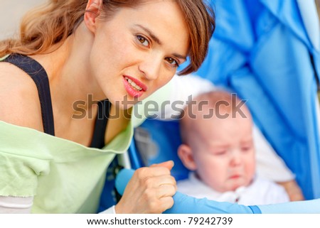 Caring young mother hugging sitting in stroller crying baby