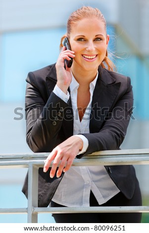 Portrait of smiling modern business woman leaning on railing and talking on mobile