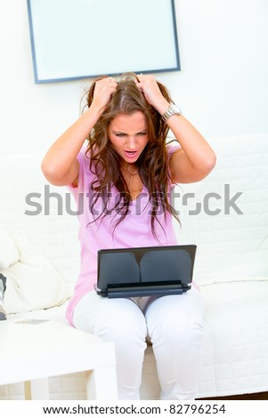 Stressed modern housewife sitting on sofa at home with laptop
