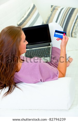 Woman sitting on sofa at home with laptop and credit card