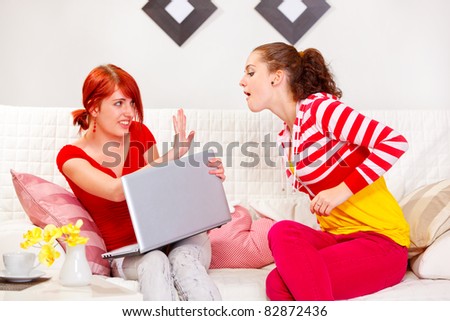 Pretty girl not allowing her girlfriend to look in laptop  at living room