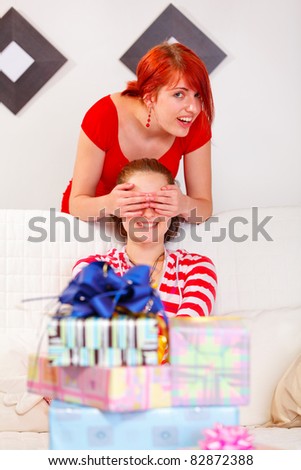 Happy girl covering girlfriends eyes for a surprise at living room