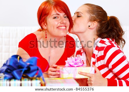 Girl presenting gift to her smiling girlfriends and kissing her