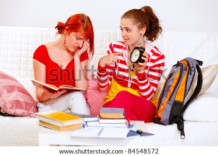 Pretty girl showing her studying girlfriends clock