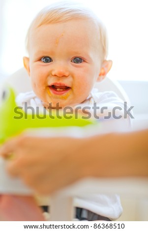 Eat smeared smiling baby sitting in baby chair