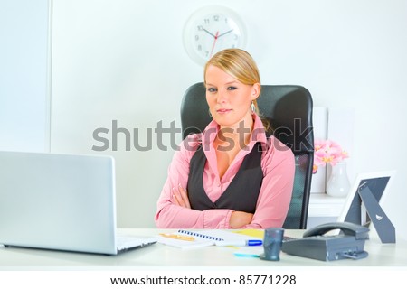 Pretty modern business woman sitting at office desk with crossed arms