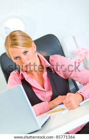 Angry modern business woman sitting at office desk with pound fist on table