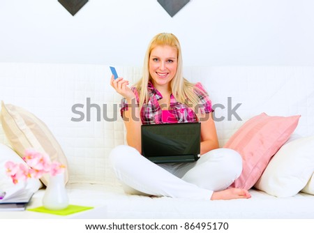 Smiling woman sitting on divan with laptop and credit card