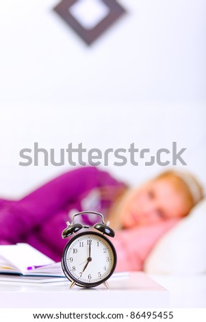 Alarm clock on table and woman laying on sofa  at home in background
