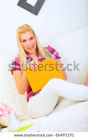 Interested pretty woman sitting on sofa and opening envelope