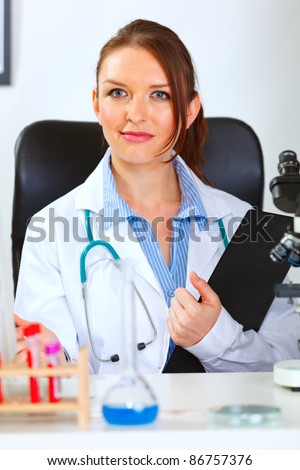 Female medical doctor sitting in cabinet with clipboard